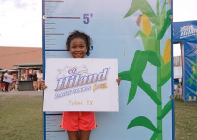 Girl holding a Hiland Dairy Tyler, TX sign in front of a life-size measuring chart